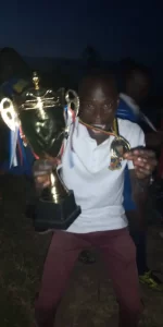 The Coach of St. Kizito Under 12 Volleyball team posing with the trophy after a win 